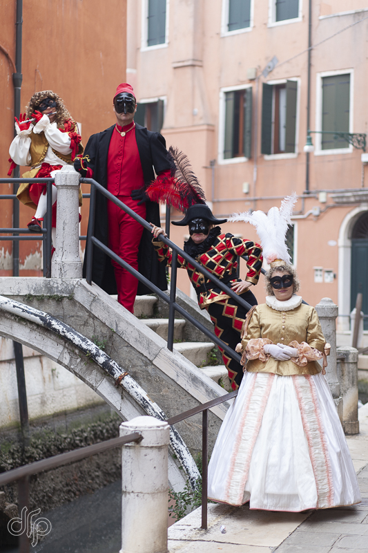 Four characters from Commedia dell'Arte posing on a small bridge in Venice, Italy