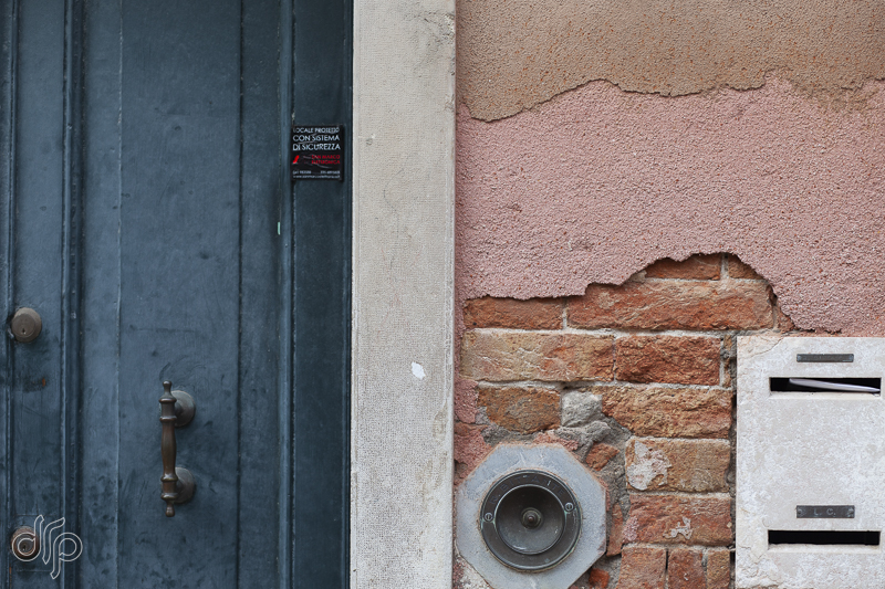 Petrol door and salmon coloured wall with doorbell and letterboxes in Venice, Italy