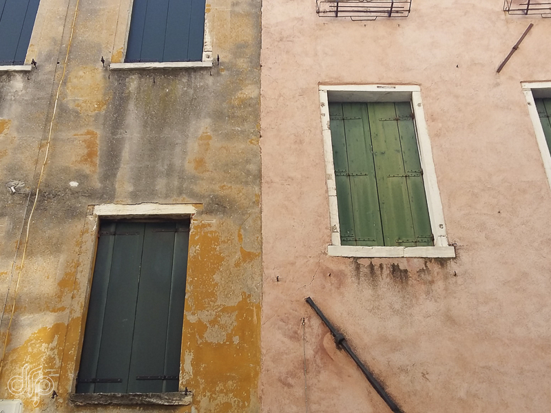 Yellow ochre and salmon colored wall abstract with green shutters in Venice, Italy